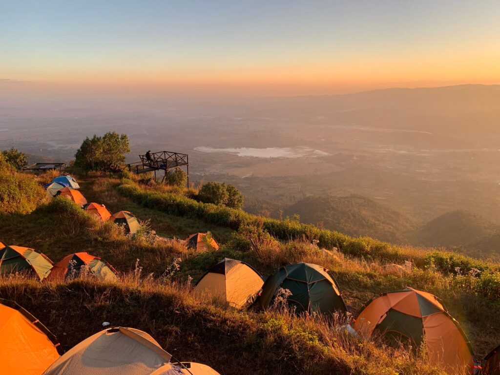 Tents pitched along a grassy ridge at sunrise above a hazy plain