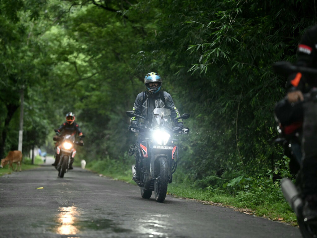 Two riders in full gear on a wet road running through thick jungle