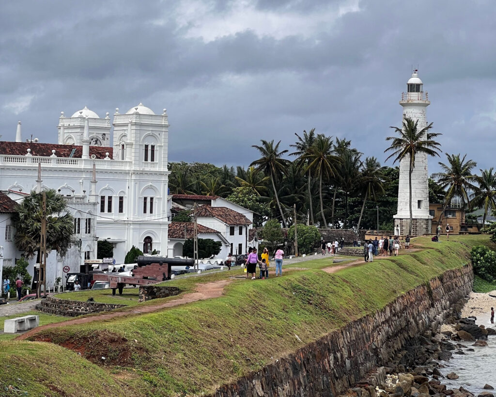 Visitors walking the rampart wall at Galle Fort, the lighthouse and the mosque behind