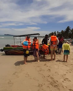 A group in life jackets beside a boat on the sand